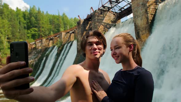 A Cute Couple on Vacation in the Forest - Man and Woman Taking a Selfie on a Background of Dam