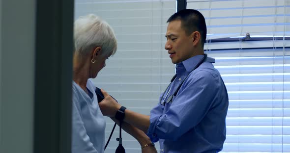 Side view of young Asian male doctor checking blood pressure of senior patient in the clinic 4k