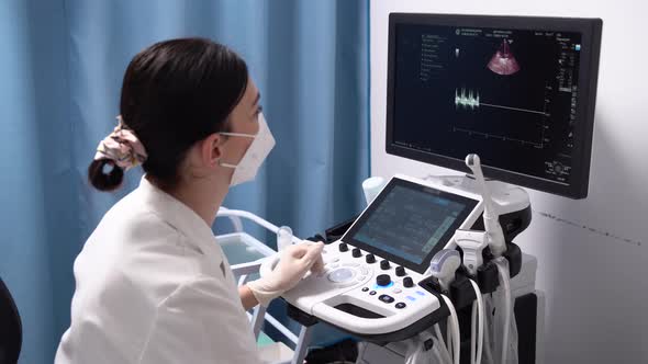 A Female Doctor in Mask and Gloves Looks at the Ultrasound Screen in a Modern Clinic