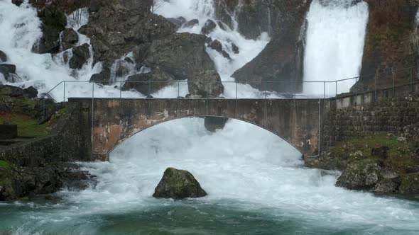 Hillside gushing waterfalls flowing under arched bridge