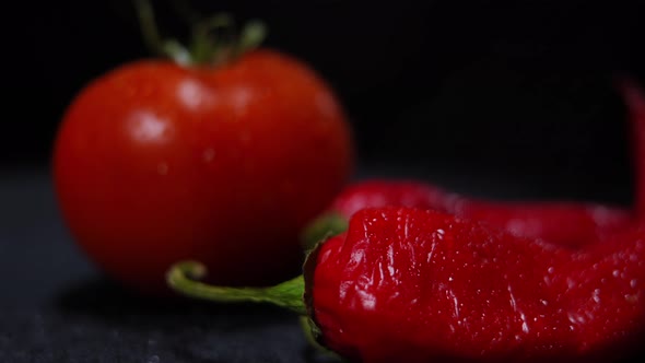 Closeup Red Hot Pepper with Water Droplets Falling in Slow Motion on Vegetable at Black Background