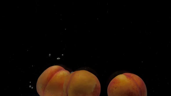 Slow Motion Three Peaches Falling Into Transparent Water on Black Background