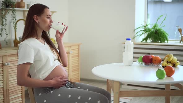 Pregnant Woman Sit at Kitchen Table Drink Milk and Touch Baby in Belly