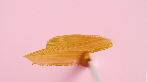 Abstract Brushstrokes of Gold Paint Brush Applied Isolated on a Pink Background