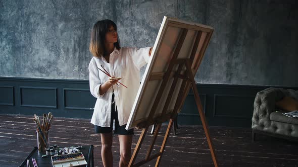 Young Woman Painter is Drawing a Picture on Canvas Using Oil Paints Palette and Paintbrushes While