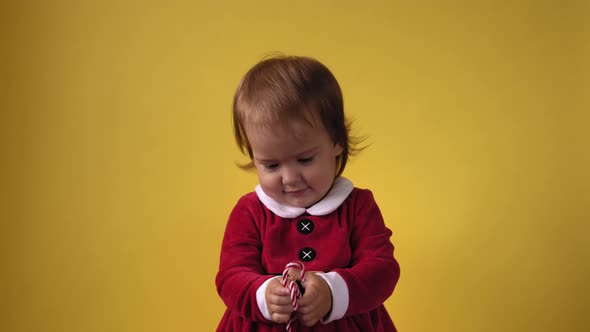 Cute Happy Cheerful Chubby Toddler Baby Girl in Santa Suit Looking On Camera At Yellow Background