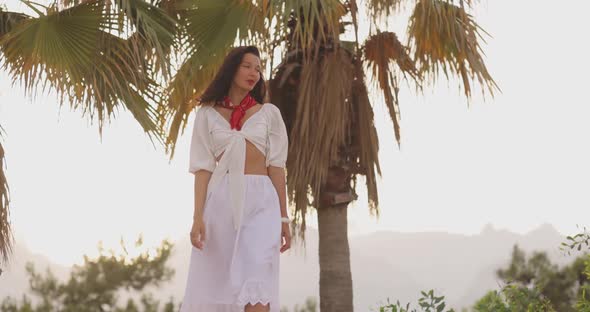 Woman in Elegant Beach Outfit Outdoors Against Palm Trees on the Background During Summer Vacations