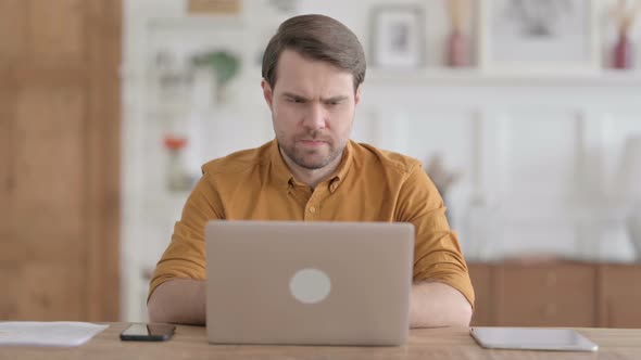 Young Man Thinking while Working on Laptop in Office