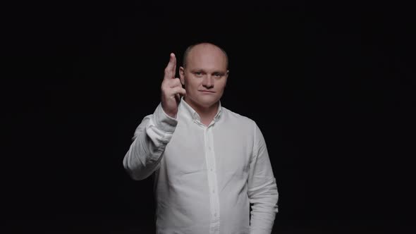 An elegant bald man in a white shirt shoots his fingers and poses for the camera on a black backgrou