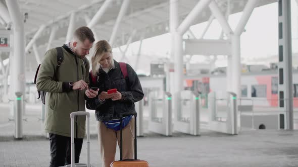 Two Passengers Are Using Smartphones Standing on Platform of Railway Station