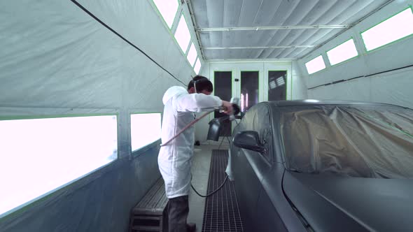 Car body painter spraying car in paint booth