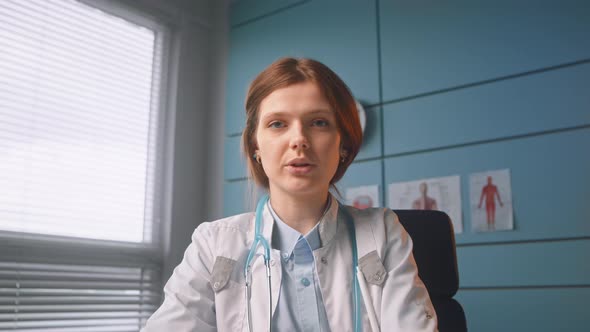 Brunette medical worker in white coat talks on video call sitting in office