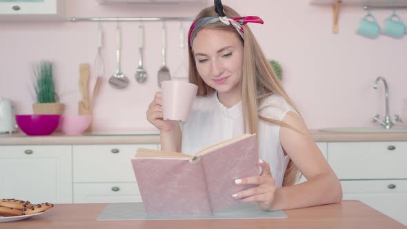 Stylish Young Woman Sitting in Kitchen Reading Book and Drinking Coffee. Happy Morning of Beautiful