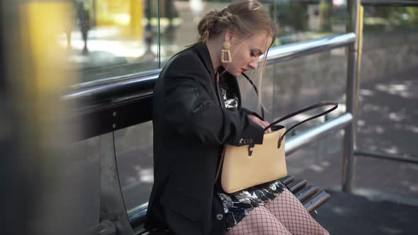 Young Beautiful Woman Searching Coronavirus Face Mask Sitting on Bus Stop and Walking Away