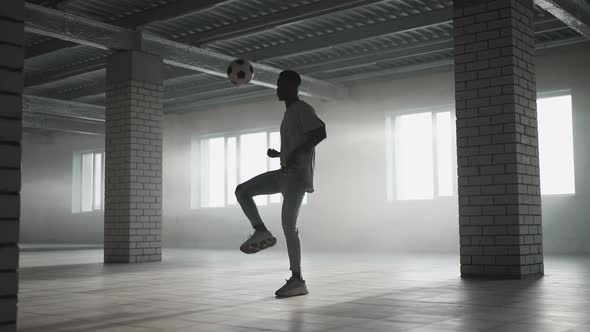 A Black Man Makes a Football Freestyle with a Ball in an Underground Parking Lot in the Sunlight