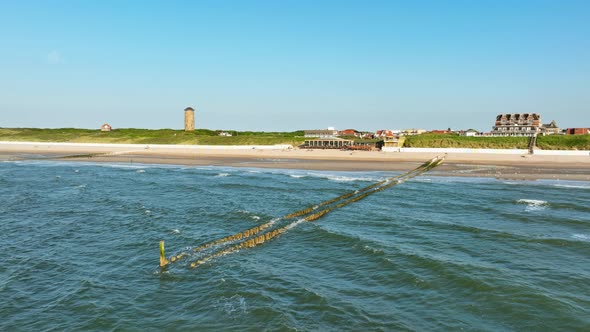 Aerial shot flying over the surf towards a beach tent outside a picturesque little coastal town on a