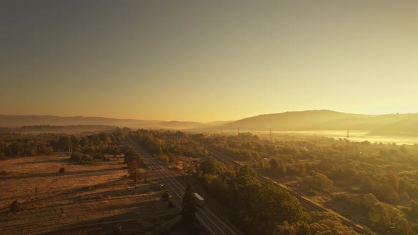 Cinematic Aerial View Fro Drone at Road with Cargo Vehicles and Railways at Sunny Sunrise in