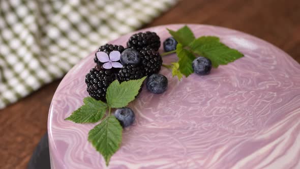 Women's Hands Decorate a Berry Mousse Cake with with Flowers on the Kitchen Table.