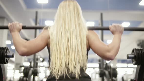 Young Beautiful Blond Female Doing Squats with Barbell