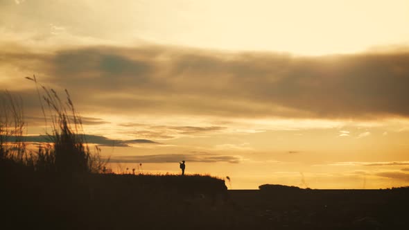 Silhouette of a Young Hiker Girl with a Backpack on Top Mountains at Sunset.