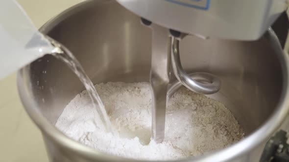 Pouring water on flour in professional Dough Kneading Machine, mixing water and flour in bakery