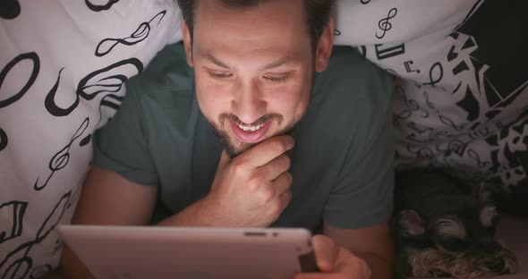 Close Up of Face of a Young Bearded and Mustashed Man Using Digital Tablet Under Blanket in His Bed