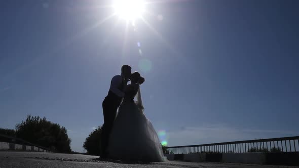 Silhouettes of newlyweds kiss gently against the backdrop of the sun