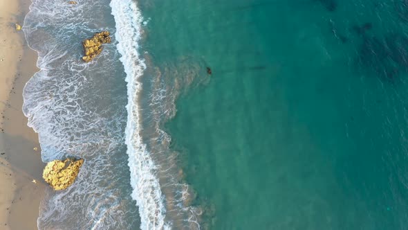 4k ariel drone shot of crystal clear blue waters along the coast of a gorgeous sunny beach.