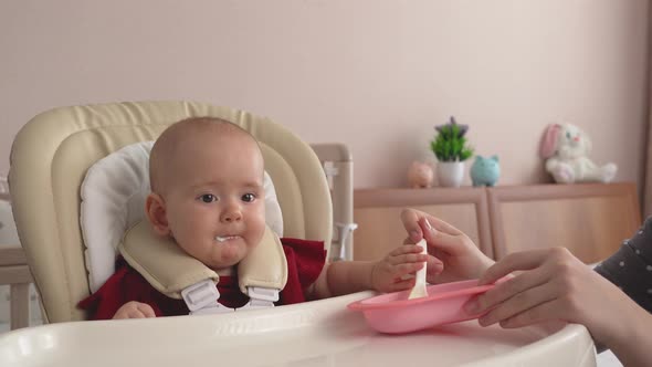 Mother feeds her newborn girl with cottage cheese. Spoon-feeding your baby with yogurt
