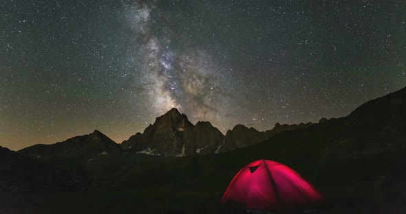 Time lapse Milky way galaxy stars rotating over the Alps, illuminated camping tent mountain peak