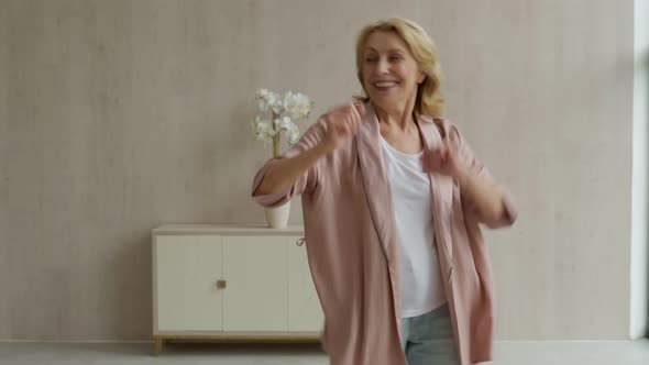 A Cheerful Elderly Woman Listens to Music and Dances in Her Living Room