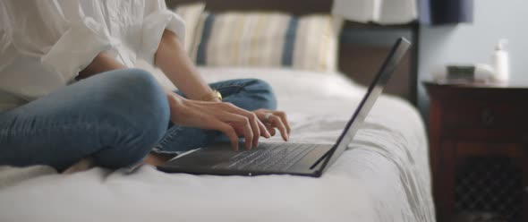 Woman hands typing something on a laptop keyboard in the bedroom.