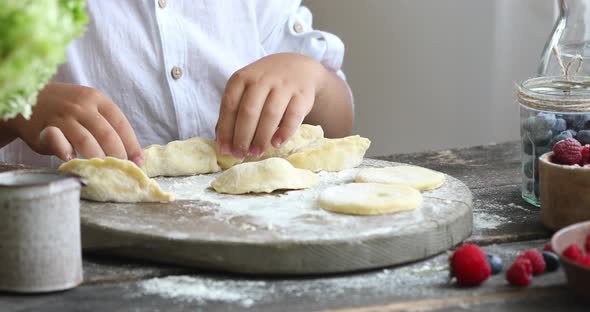 Raw pierogi with berry on a wooden board with women and child hands