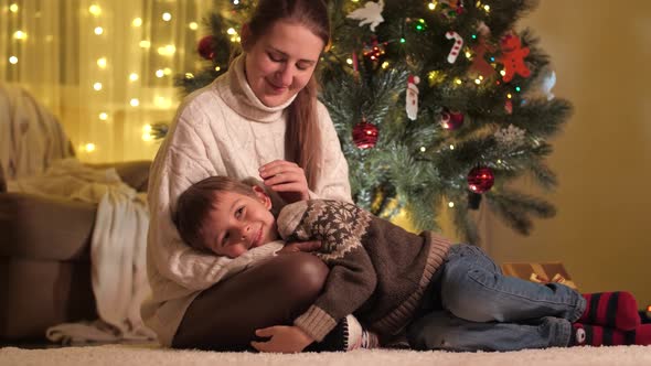 Happy Smiling Boy Lying on Mothers Lap While She Caressing Him Next to Christmas Tree