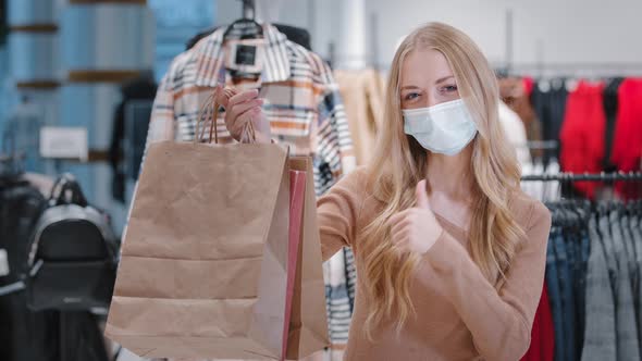 Joyful Woman Customer in Medical Mask Point Packages with Purchases Happy Girl Stand in Store