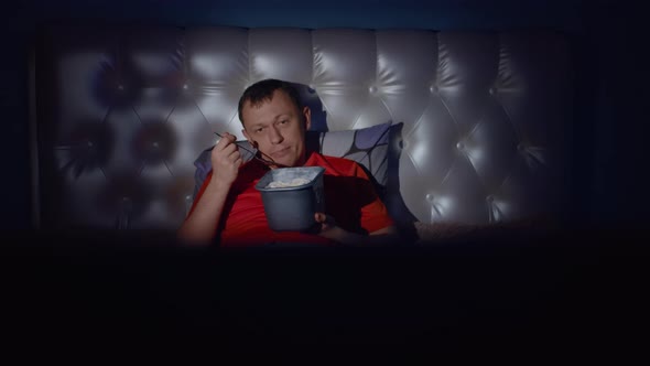 Man eating ice cream while lying on bed at night