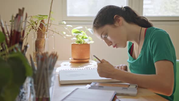 Teenage artist sitting drawing in a sketchbook in her room