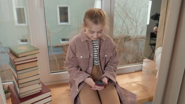 Girl Sitting on the Windowsill and Looking at the Phone