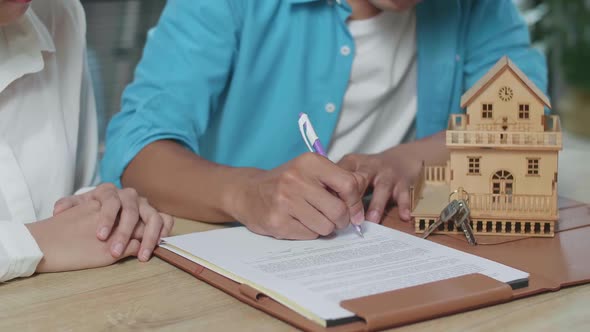 Close Up Of Man'S Hand Signing On House Purchase Contract Paper While Sitting With A Woman