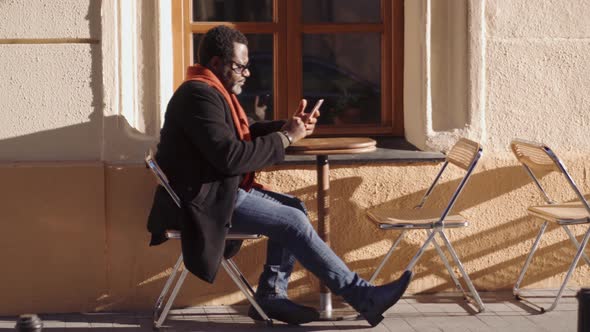 Concentrated African man in eyeglasses leafing tape by phone in cafe