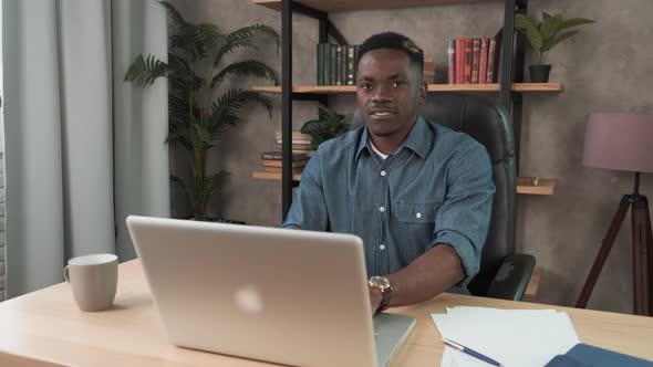 Young Black Man Employee Works in the Office at the Computer. Male Worker Looking at Camera and