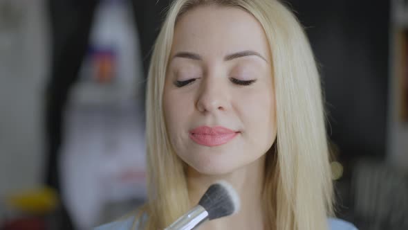 Headshot of Young Confident Gorgeous Blond Woman in Beauty Salon Smiling As Female Hand Applying