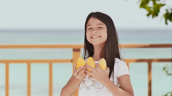 A Charming Philippine Schoolgirl Girl in a White Dress and Long Hair Positively Poses with a Mango