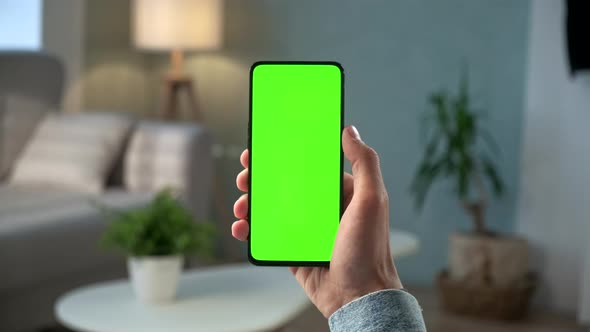 Close-up Shot of Young Man at Home Sitting on a Chair Using With Green Mock-up Screen Smartphone