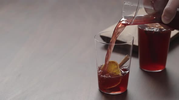 Slow Motion Man Hand Serving Mulled Wine in Thin Tumbler Glasses on Walnut Table