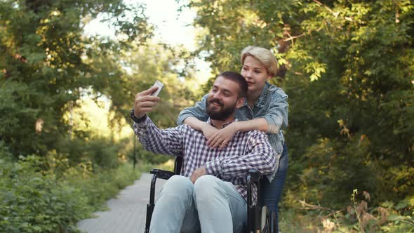 Woman Hugs Man in Wheelchair Who is Taking Selfie