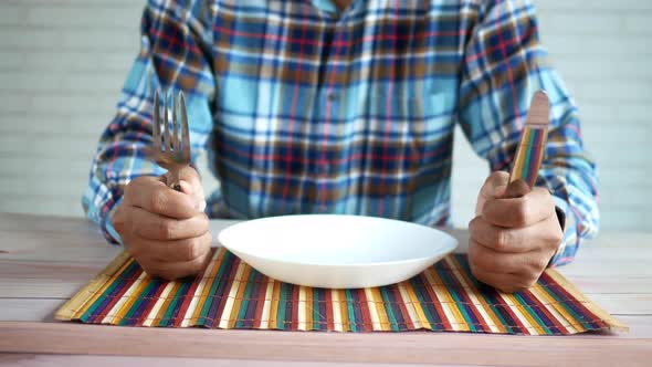 Hand Holding Cutlery with Empty Plate on Wooden Table