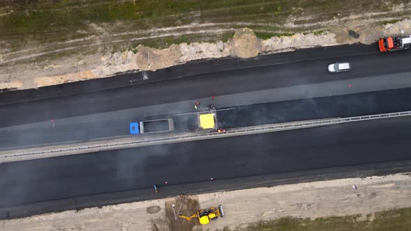 Drone move down to the yellow road paver and workers. Roadworks on the motorway