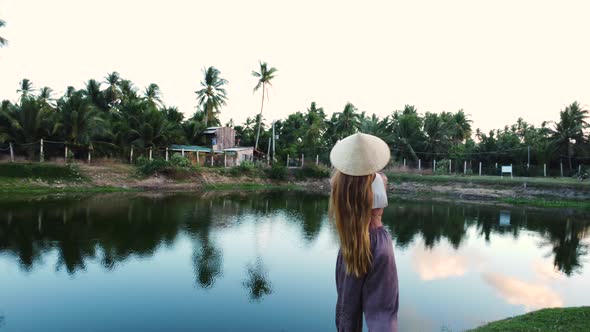 Attractive woman with conical hat fishing in tropical Vietnam lake, orbit view