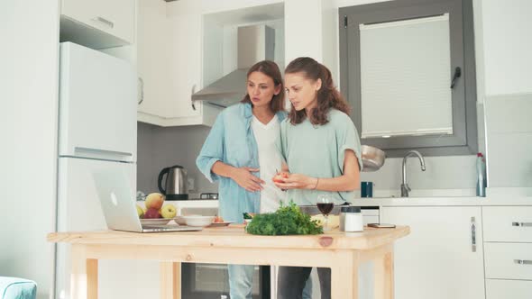 Two Young Caucasian Women Talking with Friends Via the Internet While Cooking.